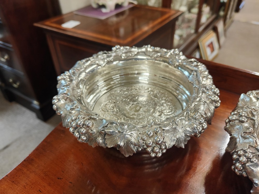 A pair of circular Georgian silver wine coasters featuring intricate cast grape and vine leaf borders with turned wooden bases. View VI