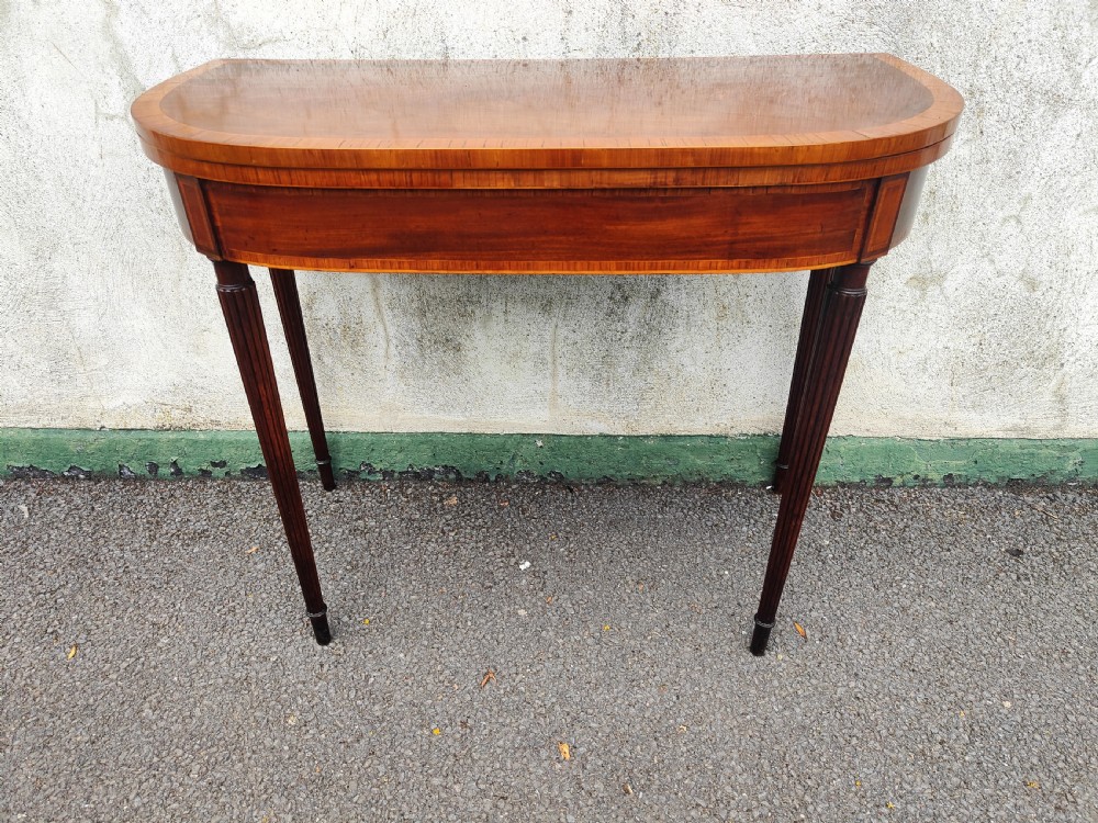 A Georgian mahogany demilune card table featuring satinwood crossbanding along the folded top and fluted tapered legs. View II