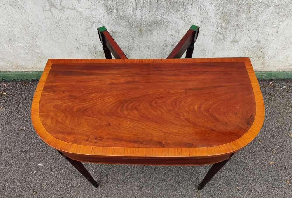 A Georgian mahogany demilune card table featuring satinwood crossbanding along the folded top and fluted tapered legs. View III