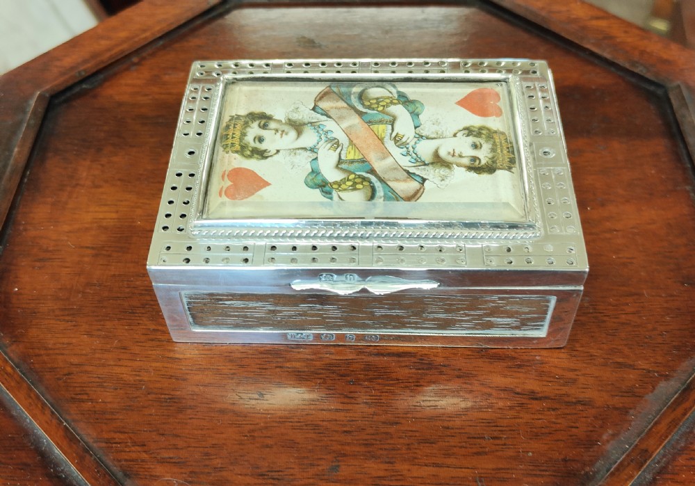 A rectangular late Victorian sterling silver cribbage box featuring a central glazed Queen of Hearts playing card surrounded by a pegboard border.