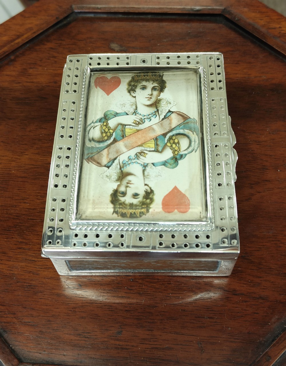 A rectangular late Victorian sterling silver cribbage box featuring a central glazed Queen of Hearts playing card surrounded by a pegboard border. View VI