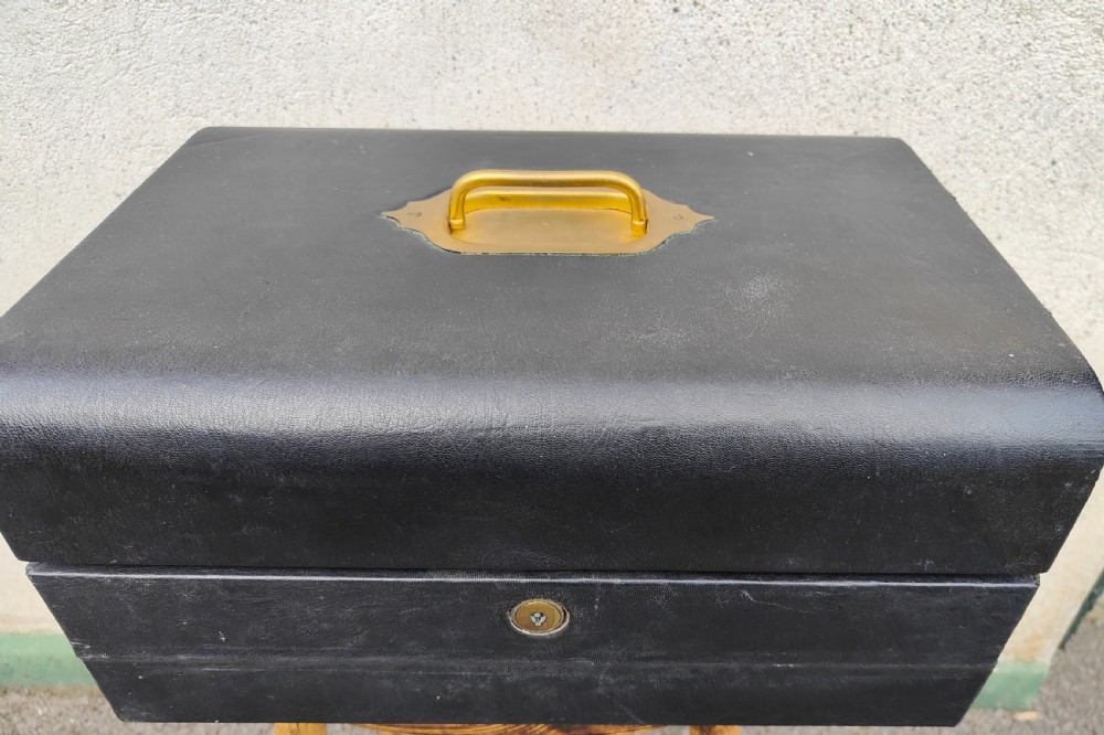 A rectangular black leather-bound writing box featuring a brass handle inset on top and a circular brass keyhole on the front.