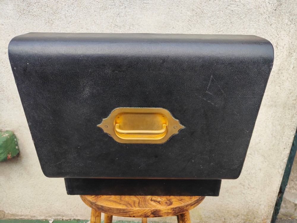 A rectangular black leather-bound writing box featuring a brass handle inset on top and a circular brass keyhole on the front. View VII