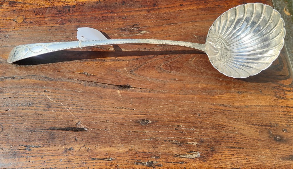 An antique sterling silver ladle featuring a detailed shell-shaped bowl and a long handle decorated with delicate bright-cut engraving.