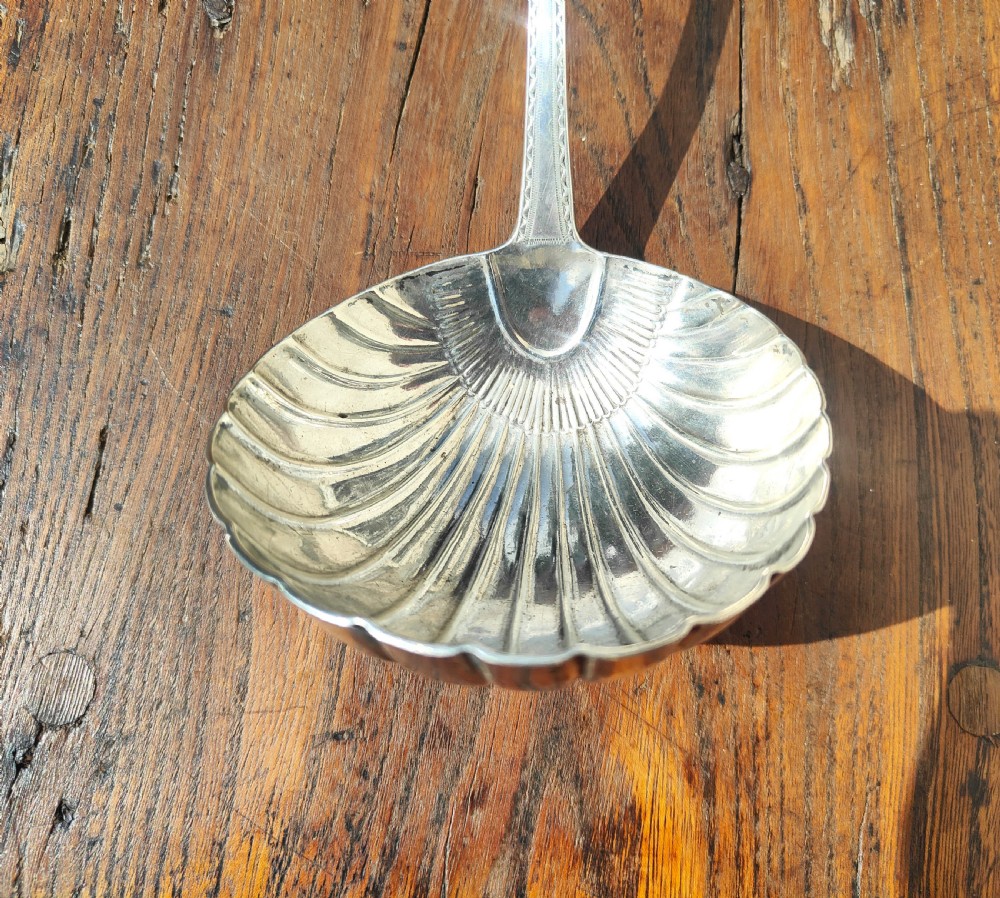 An antique sterling silver ladle featuring a detailed shell-shaped bowl and a long handle decorated with delicate bright-cut engraving. View II