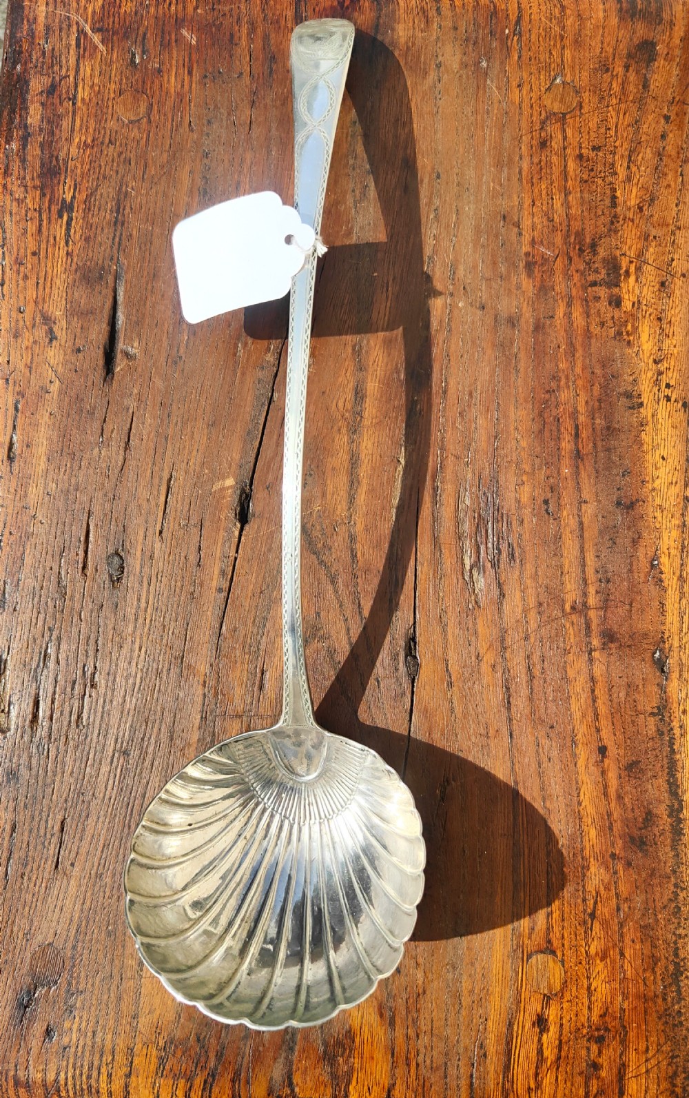 An antique sterling silver ladle featuring a detailed shell-shaped bowl and a long handle decorated with delicate bright-cut engraving. View VI