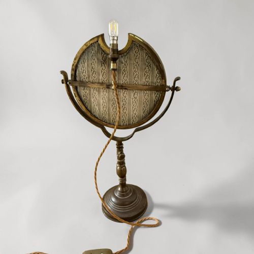 fig 1. An Edwardian adjustable brass shaving mirror featuring a turned pedestal stem, round weighted base, and a swivelling circular mirror frame with an integrated light fitting.