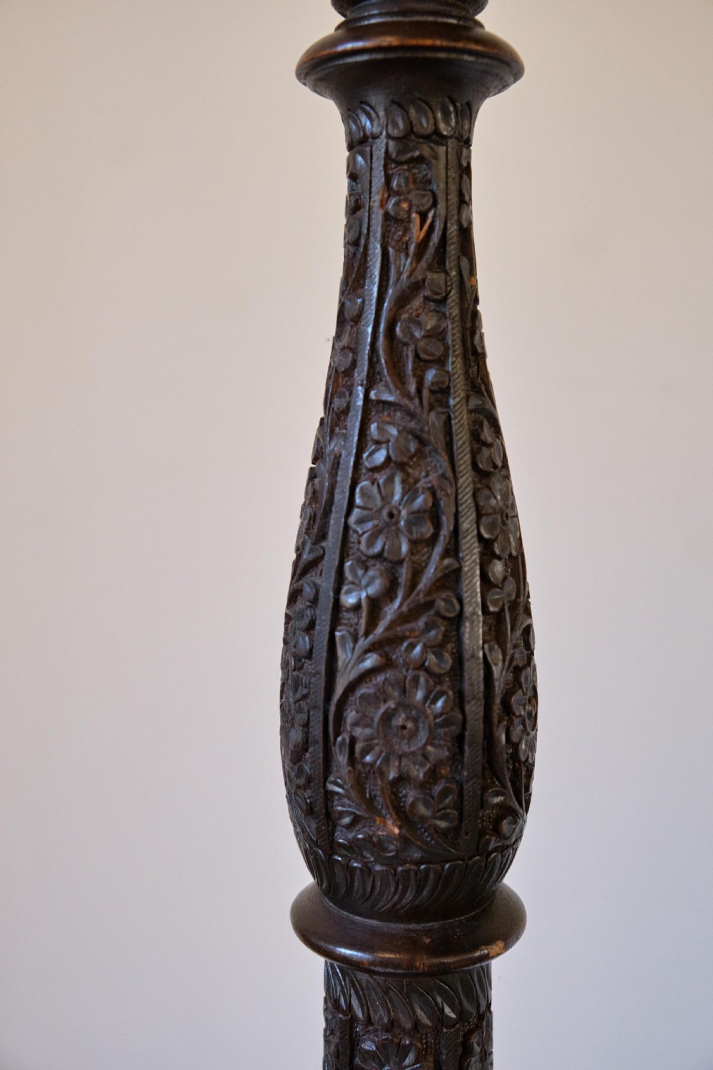 An Anglo-Indian dark wood standard lamp featuring intricate foliate hand-carving along the column and circular base, topped with a brass bulb socket. View II