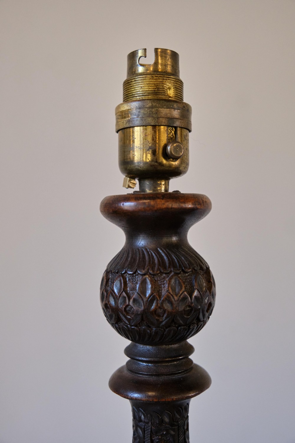 An Anglo-Indian dark wood standard lamp featuring intricate foliate hand-carving along the column and circular base, topped with a brass bulb socket. View III