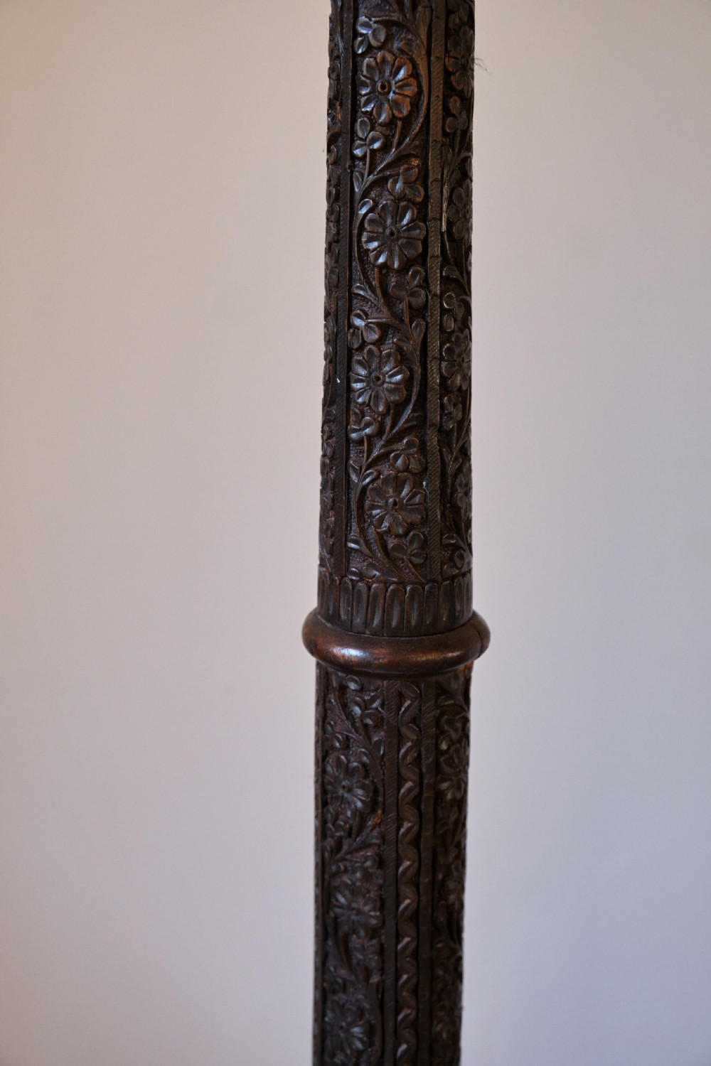 An Anglo-Indian dark wood standard lamp featuring intricate foliate hand-carving along the column and circular base, topped with a brass bulb socket. View IV