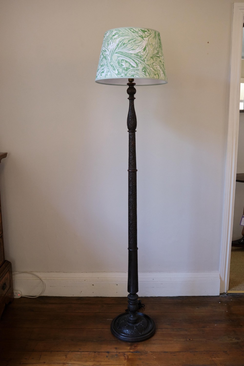 An Anglo-Indian dark wood standard lamp featuring intricate foliate hand-carving along the column and circular base, topped with a brass bulb socket. View V