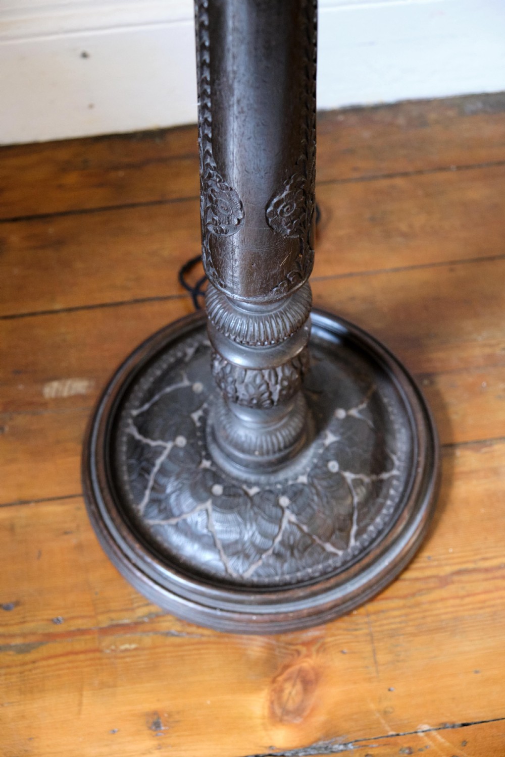 An Anglo-Indian dark wood standard lamp featuring intricate foliate hand-carving along the column and circular base, topped with a brass bulb socket. View VI