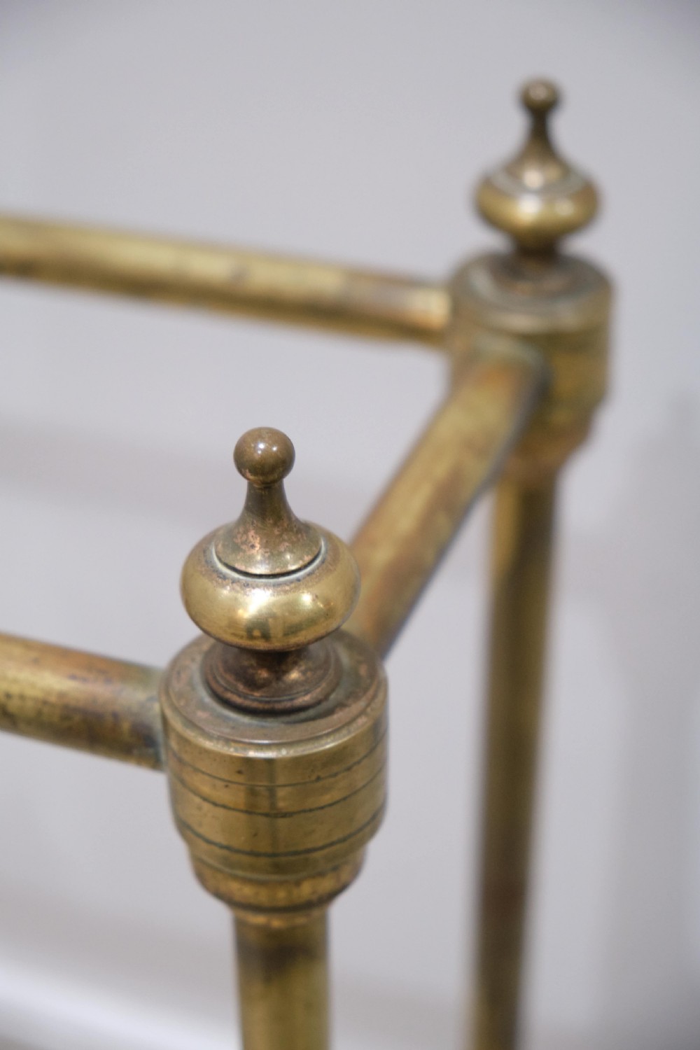 A Victorian brass umbrella stand featuring turned uprights with finials, a divided top rail, and a rectangular white drip tray base. View III