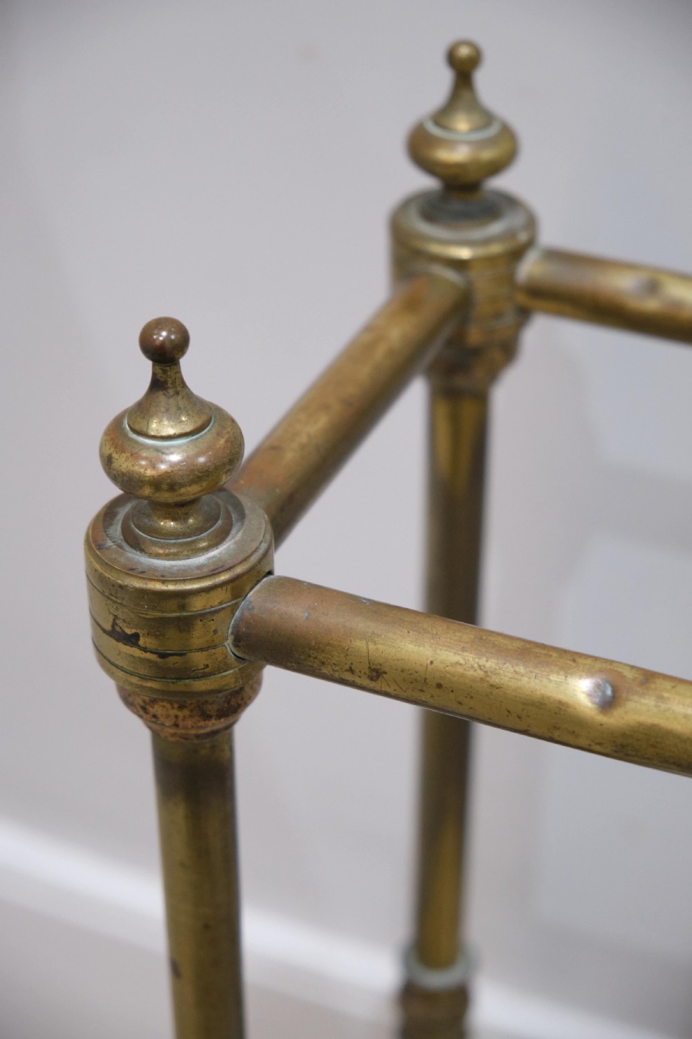 A Victorian brass umbrella stand featuring turned uprights with finials, a divided top rail, and a rectangular white drip tray base. View IV