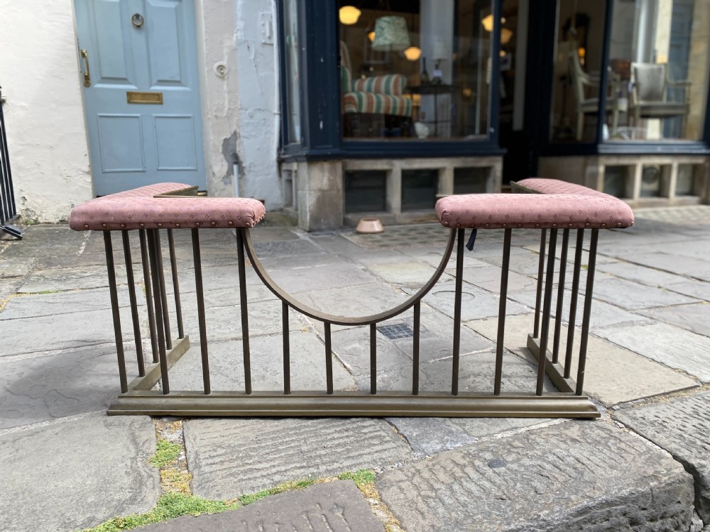 An Edwardian brass club fender featuring vertical metal spindles, a dip-centre front bar, and two pink upholstered padded corner seats. View II