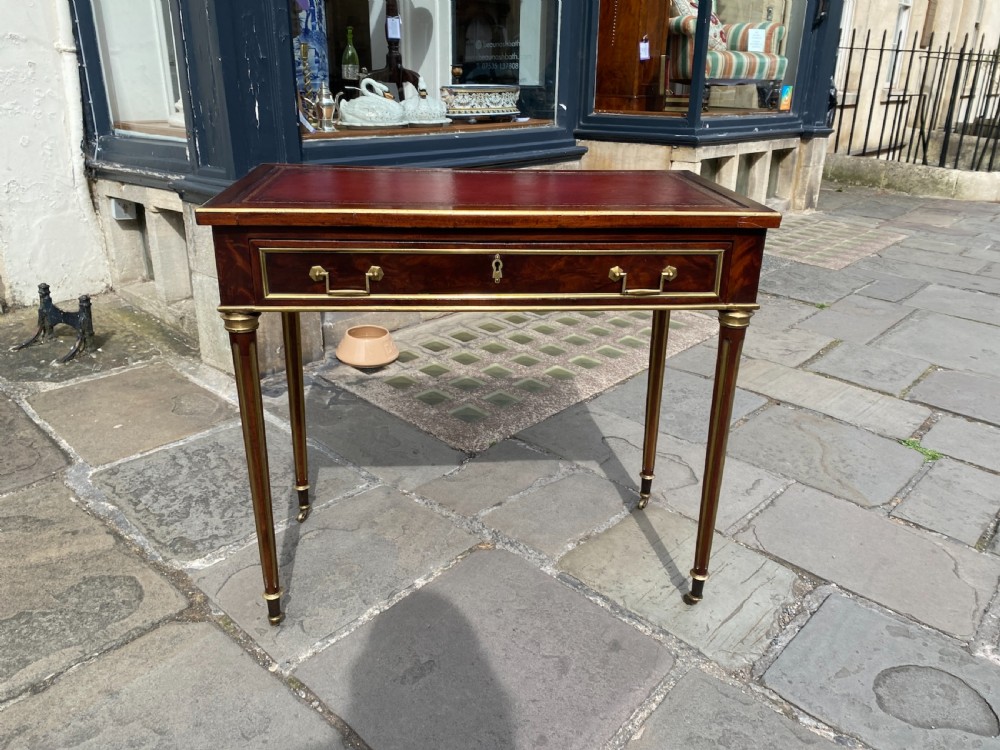 A French mahogany writing table featuring a red leather inset top, brass mouldings, a lockable single drawer, and fluted tapered legs. View III