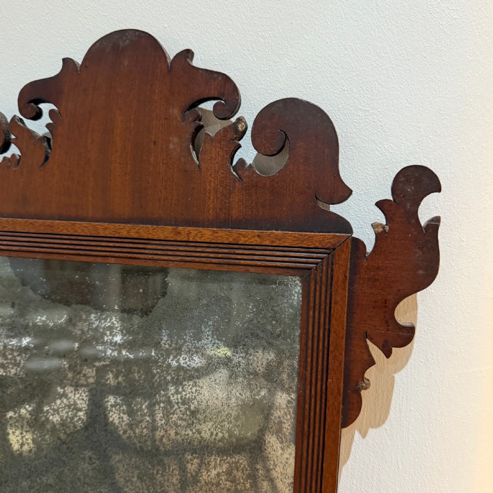 A Georgian mahogany fretwork wall mirror featuring a scrollwork cresting and heavily foxed mirror glass. View II