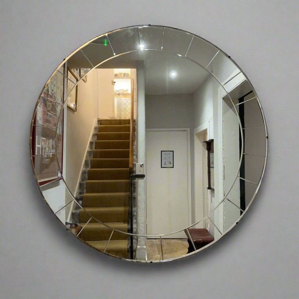 A circular Art Deco wall mirror featuring a segmented geometric glass outer border and a frameless design.