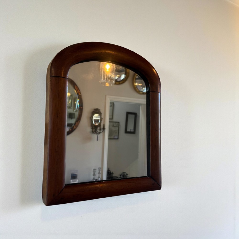 A Victorian wall mirror featuring an arched frame crafted from dark mahogany timber.