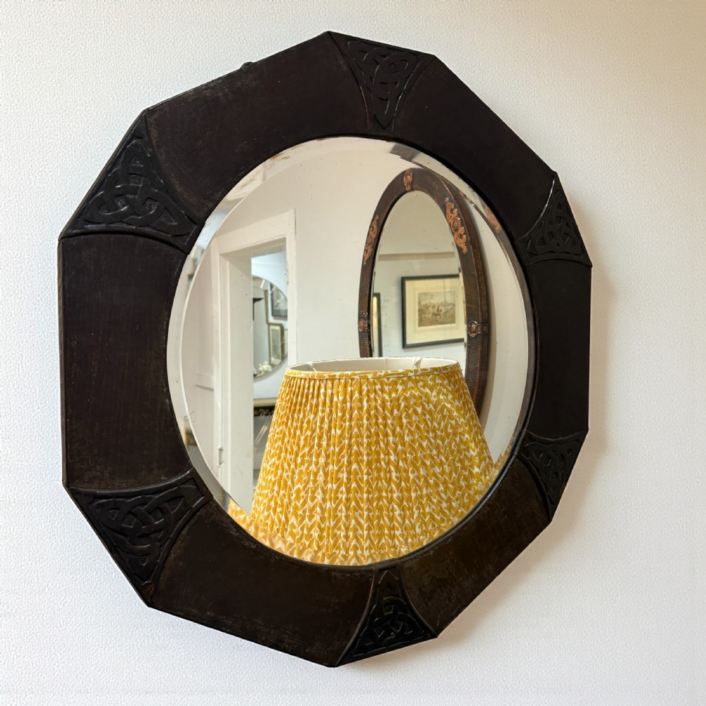 An octagonal wall mirror featuring a dark patinated copper frame decorated with embossed Celtic knotwork corners and a central circular bevelled glass plate.