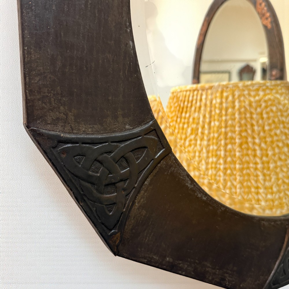 An octagonal wall mirror featuring a dark patinated copper frame decorated with embossed Celtic knotwork corners and a central circular bevelled glass plate. View II