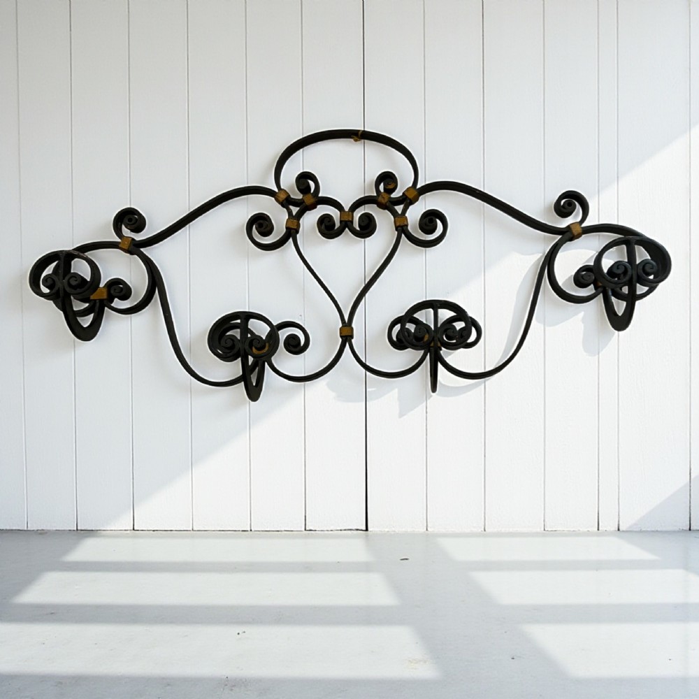 A large wall-mounted French wrought iron coat rack featuring elaborate scrolling motifs and four multi-prong hooks with gold-tone brass accents.