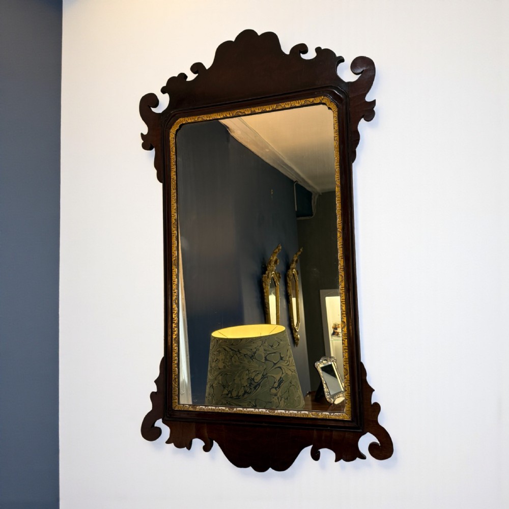 A Georgian mahogany wall mirror featuring scroll-carved fretwork cresting, a shaped apron, and an inner gilded slip.