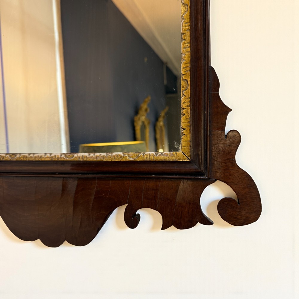 A Georgian mahogany wall mirror featuring scroll-carved fretwork cresting, a shaped apron, and an inner gilded slip. View II
