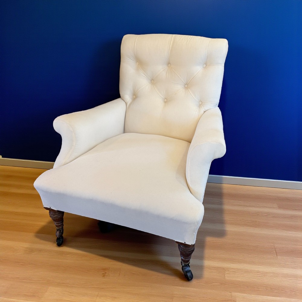 A pair of 19th-century Howard-style armchairs upholstered in cream fabric featuring deep button-backed tufting and turned dark walnut front legs on brass castors. View II