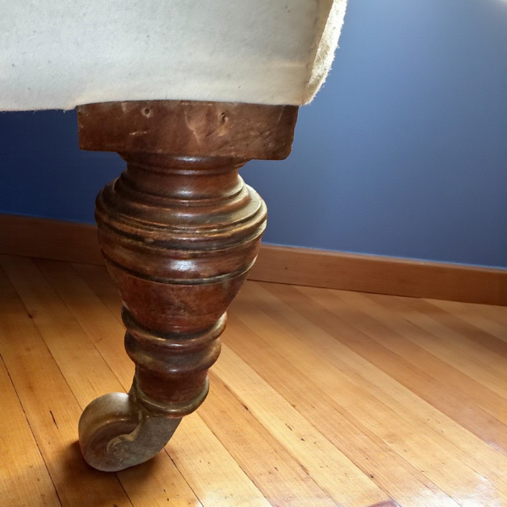 A pair of 19th-century Howard-style armchairs upholstered in cream fabric featuring deep button-backed tufting and turned dark walnut front legs on brass castors. View IV