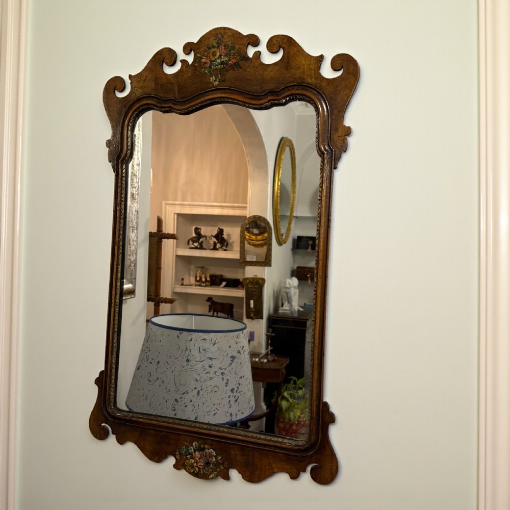 An antique Georgian style wall mirror featuring a scrolled walnut veneered frame with painted floral details on the top crest and bottom apron.