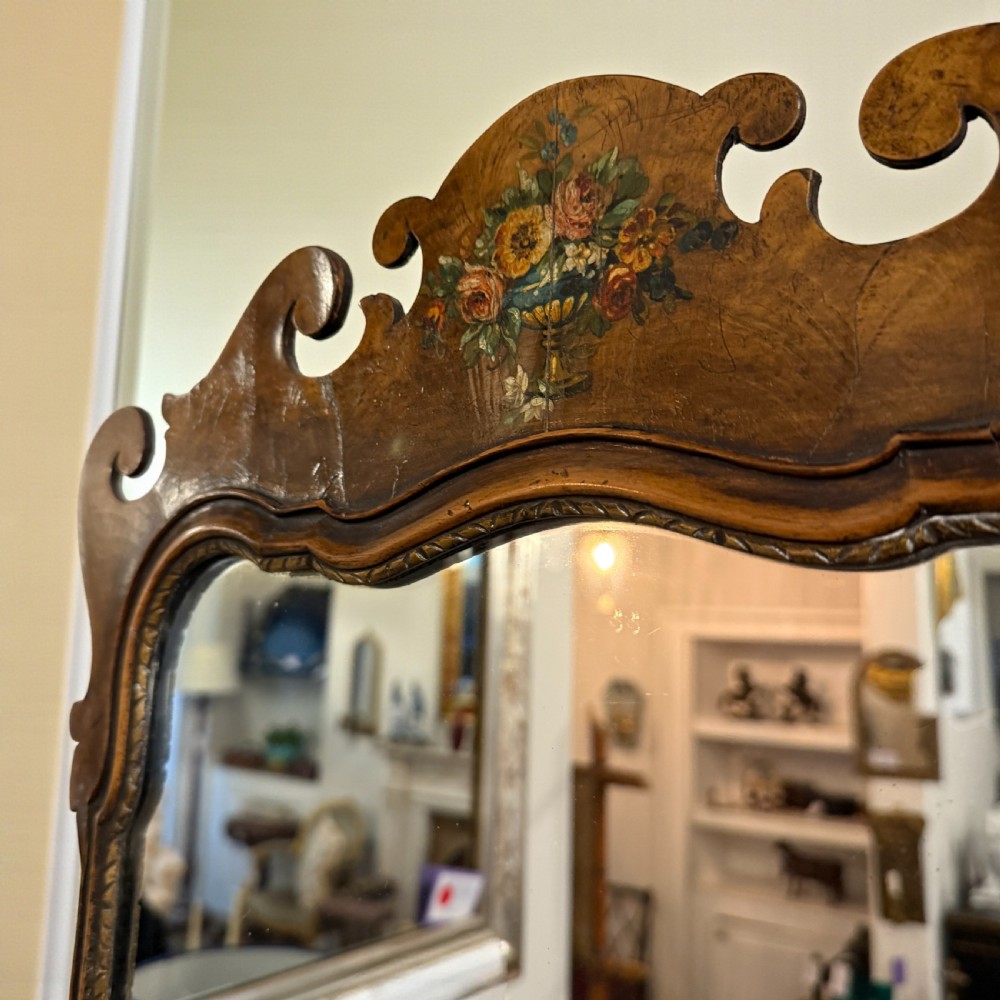 An antique Georgian style wall mirror featuring a scrolled walnut veneered frame with painted floral details on the top crest and bottom apron. View II