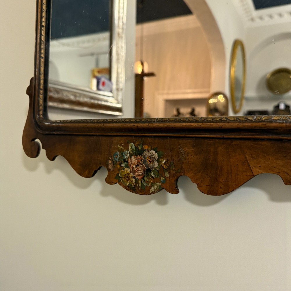 An antique Georgian style wall mirror featuring a scrolled walnut veneered frame with painted floral details on the top crest and bottom apron. View III