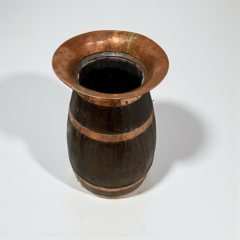 A coopered dark wood barrel stick stand featuring broad riveted copper binding bands and a flared copper top rim.