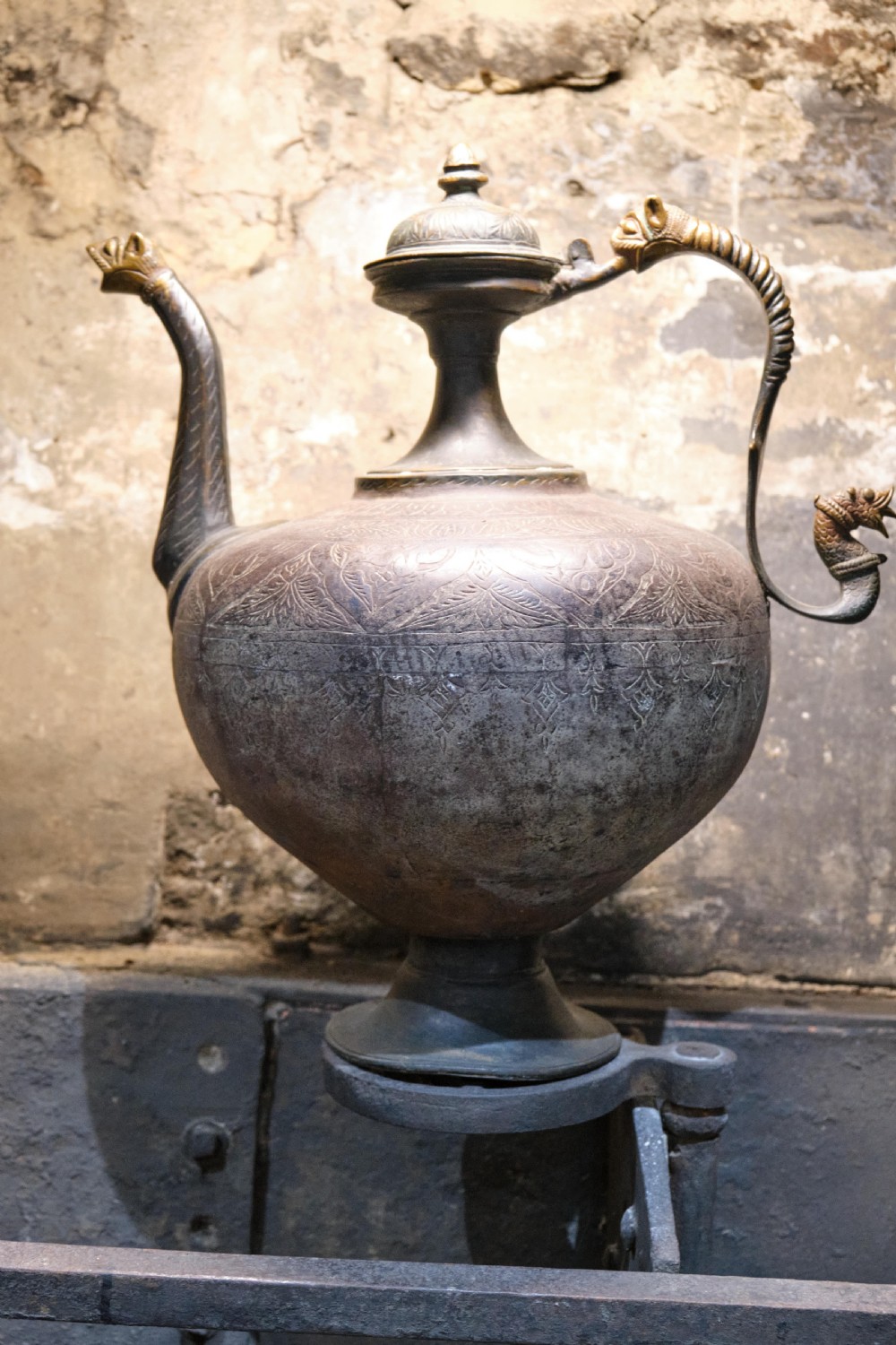 A patinated 19th-century Indian bronze ewer featuring hand-engraved floral motifs, a pedestal foot, and zoomorphic spout and handle details.