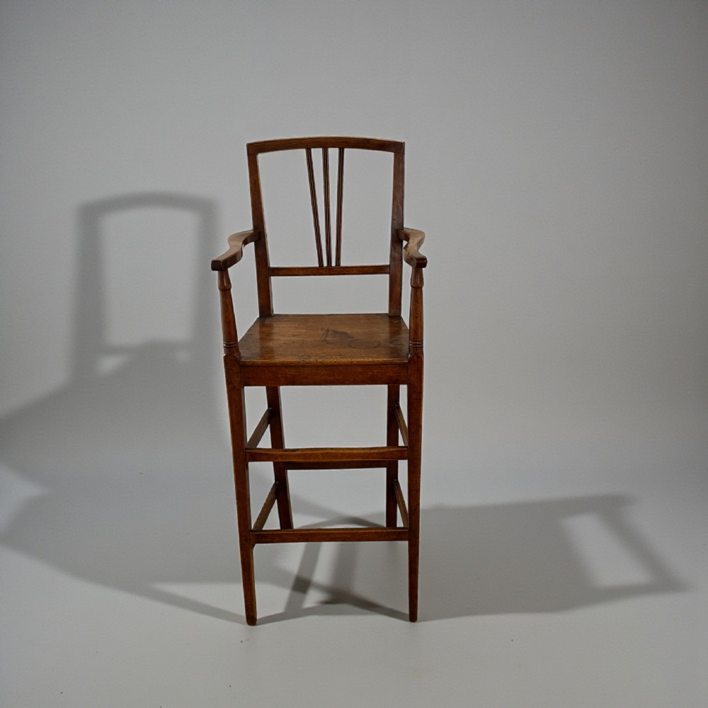 A Regency period wooden childrens high chair featuring a three-slat backrest, raised armrests with turned supports, and tall legs connected by stretchers.