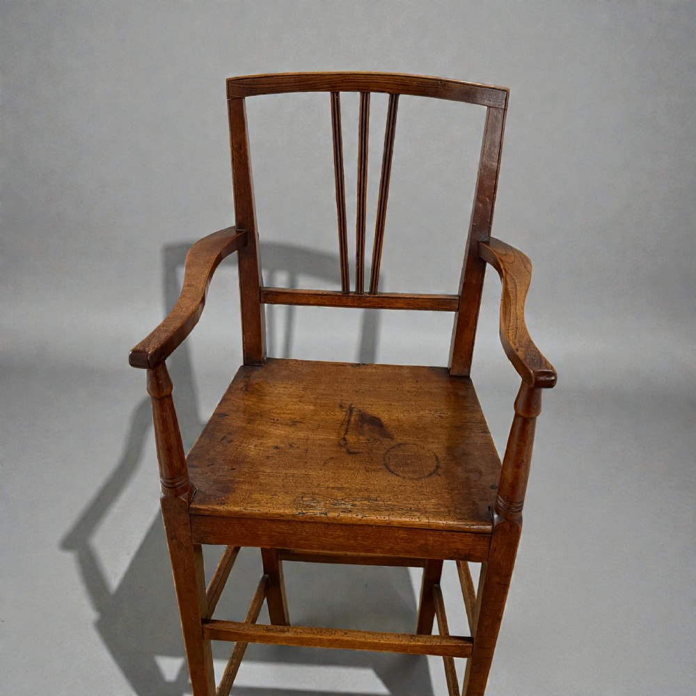 A Regency period wooden childrens high chair featuring a three-slat backrest, raised armrests with turned supports, and tall legs connected by stretchers. View II