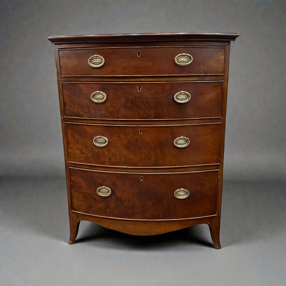 A small Georgian style mahogany bowfront chest of four drawers featuring brass oval drop handles and splayed bracket feet.