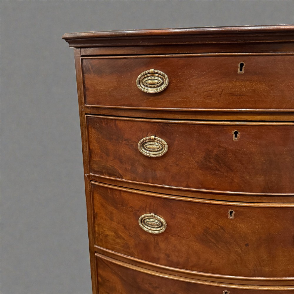A small Georgian style mahogany bowfront chest of four drawers featuring brass oval drop handles and splayed bracket feet. View II