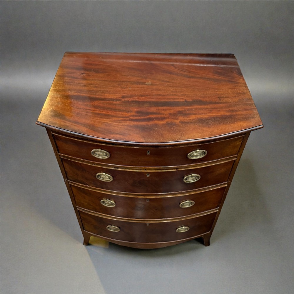 A small Georgian style mahogany bowfront chest of four drawers featuring brass oval drop handles and splayed bracket feet. View III