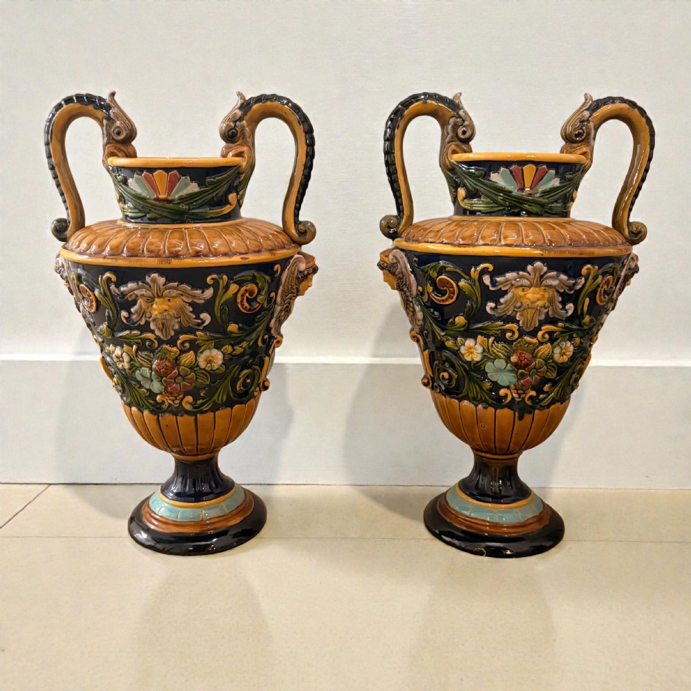 Pair of 19th-century Renaissance Revival majolica ceramic urns with dragon handles, mascaron reliefs, and polychrome glazes.