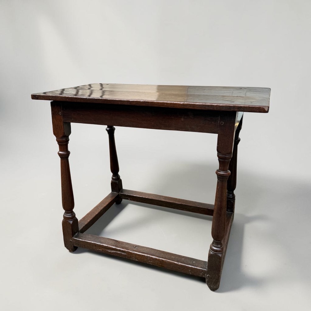 A 17th-century dark oak joint stool featuring turned legs, pegged mortise and tenon construction, and a rectangular top over low perimeter box stretchers.