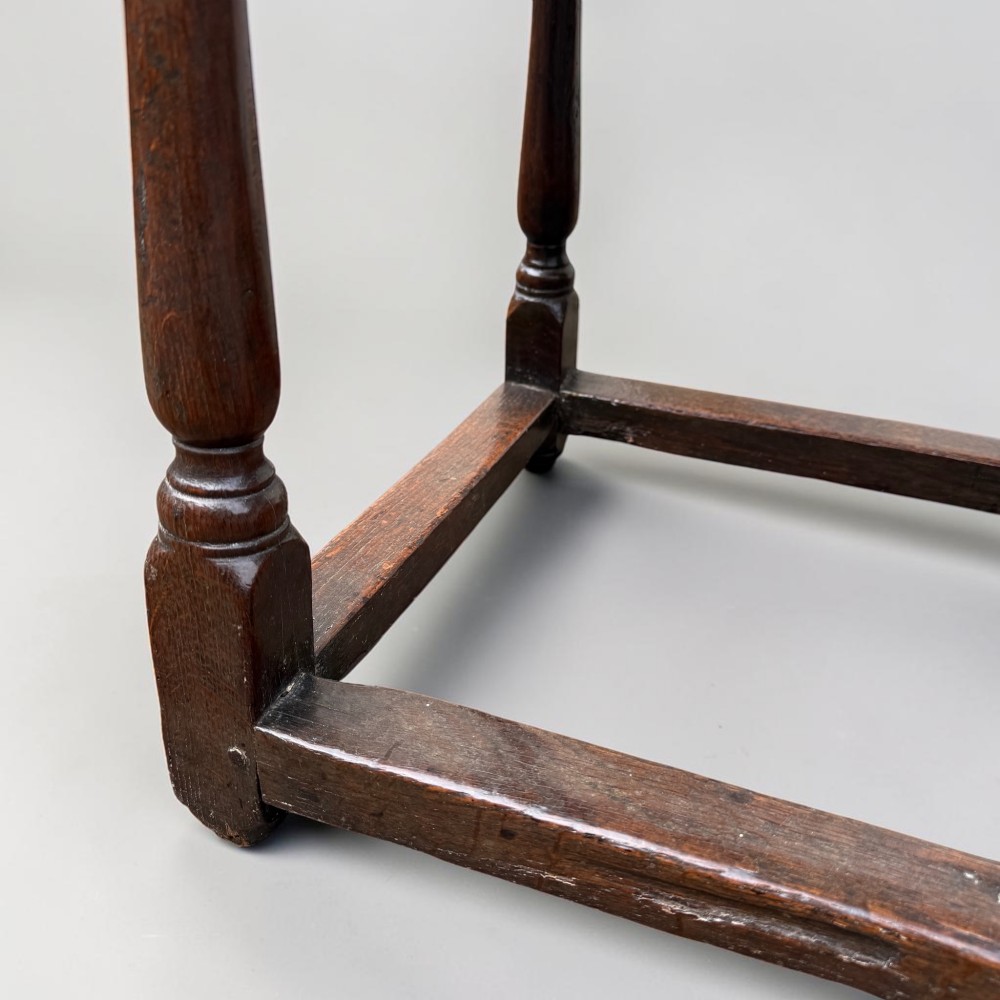 A 17th-century dark oak joint stool featuring turned legs, pegged mortise and tenon construction, and a rectangular top over low perimeter box stretchers. View III