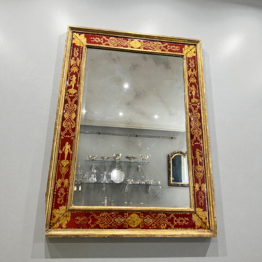 A rectangular wall mirror featuring a giltwood frame surrounding a broad red verre eglomise glass border decorated with gold scrollwork and classical figures. View III