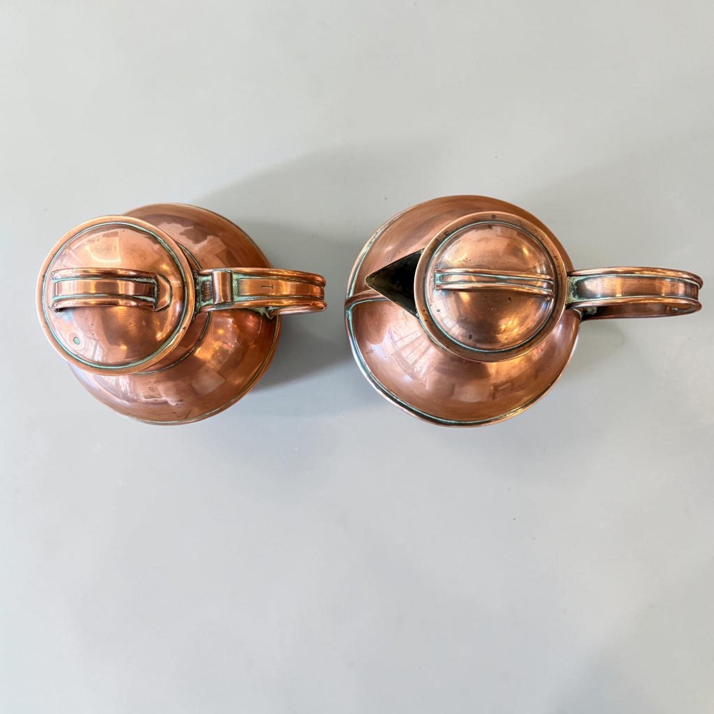 A pair of round copper Jersey milk jugs featuring fitted lids with top loop handles and wide pouring spouts. View IV