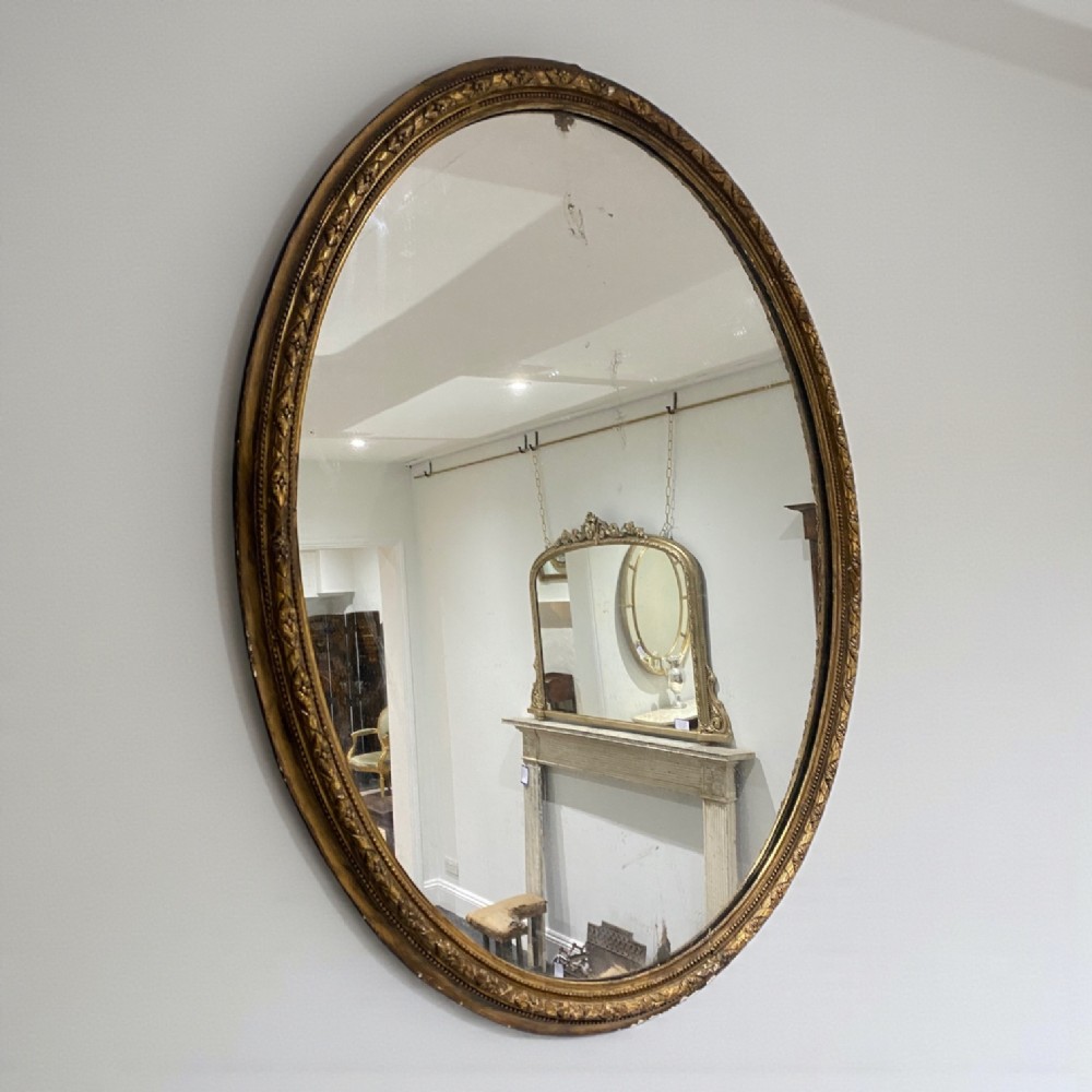 A large vertical oval wall mirror featuring an intricate gold giltwood frame with classical moulded detailing.