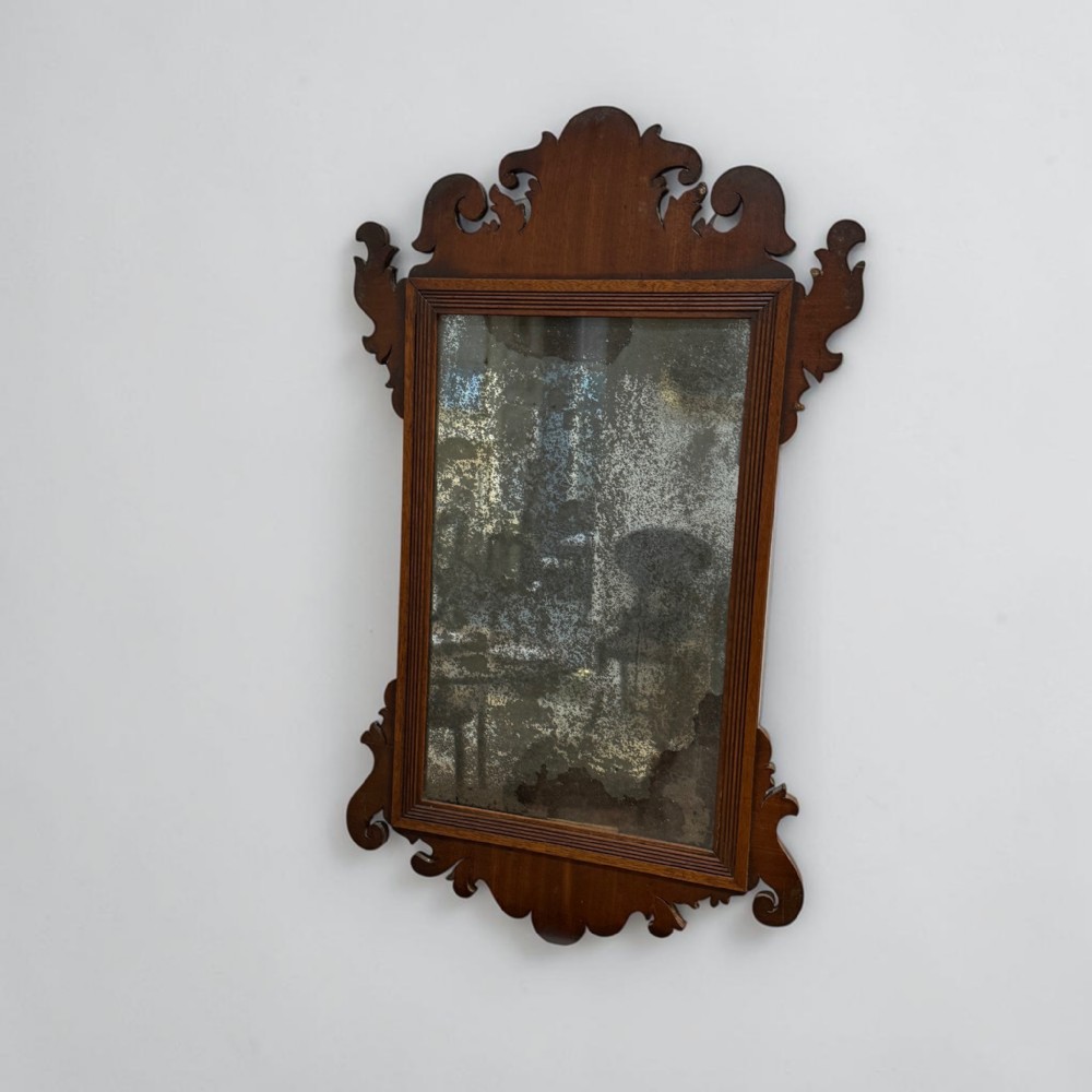 A Georgian mahogany wall mirror featuring decorative fret-carved scrollwork along the upper crest and lower apron surrounding a rectangular foxed mirror glass.