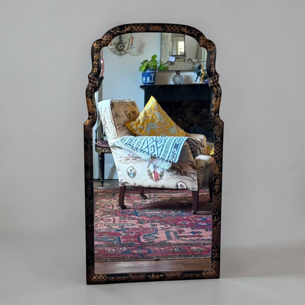 An early 20th-century rectangular wall mirror featuring an arched top and a black lacquer frame decorated with detailed gilt Chinoiserie motifs.