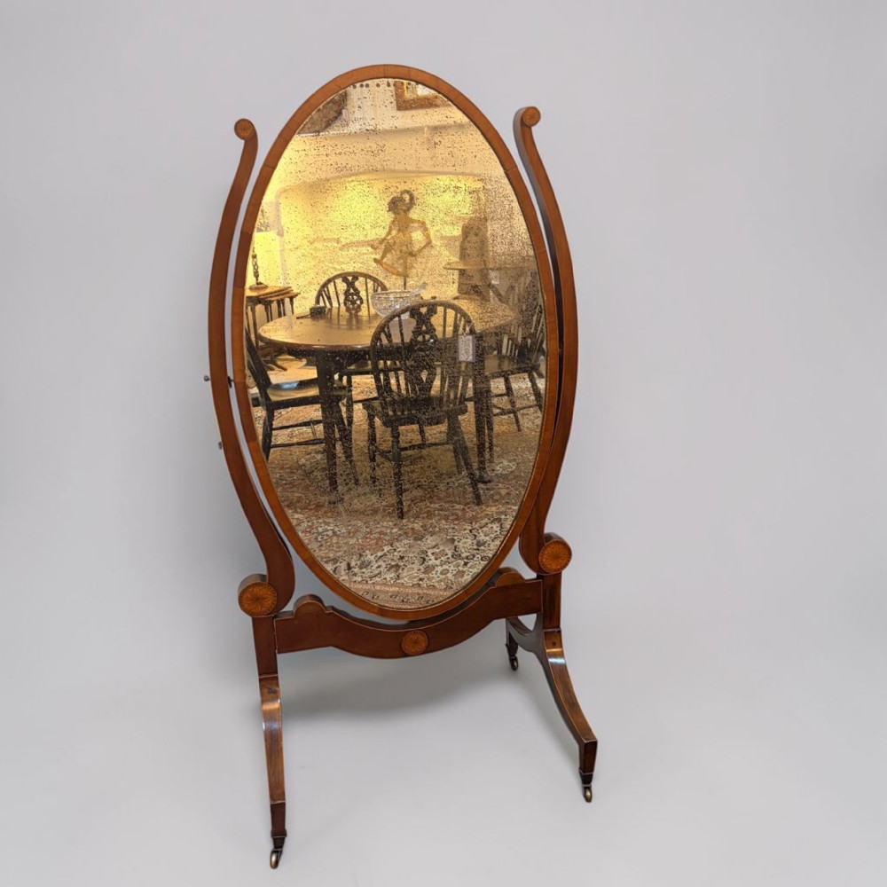 A 19th-century oval mahogany cheval mirror featuring turned side supports, inlaid patera details, and splayed legs on brass castors.