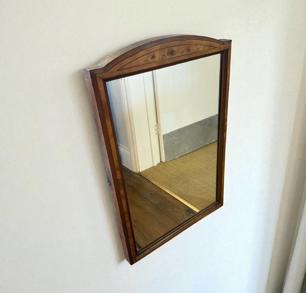 A rectangular antique wooden wall mirror featuring a gently arched top frame detailed with walnut, yew, and mahogany veneers.